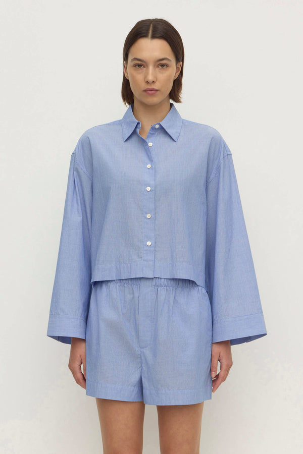Woman wearing a blue and white stripe cropped shirt, with matching mini shorts, against a plain white background.