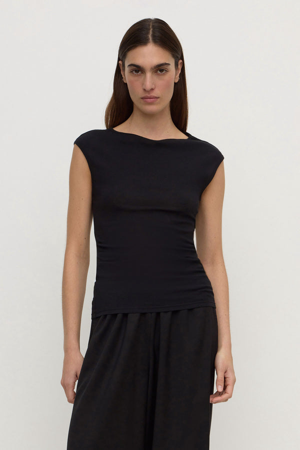 A woman wearing a black sleeveless top with a wide boat neckline and fitted waist, paired with black wide-leg pants, against a plain white background.
