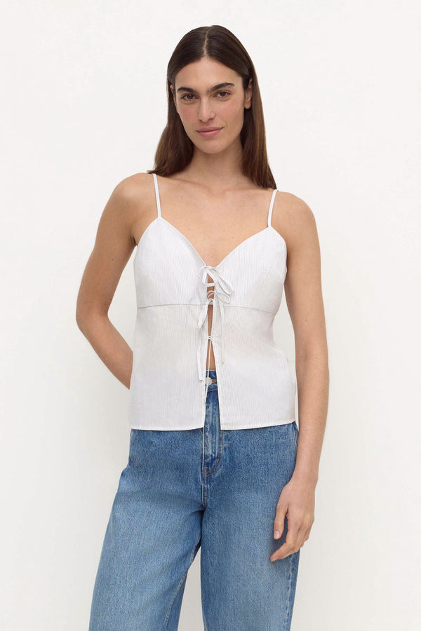 A woman wearing a blue and white stripe camisole top with a front tie closure, paired with blue jeans, against a plain white background.