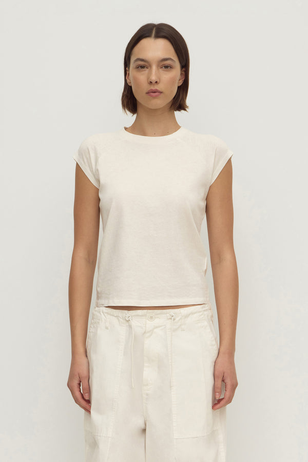 A woman wearing an off-white cap sleeve raglan style tee with white utility style drawcord pants, set against a white background.